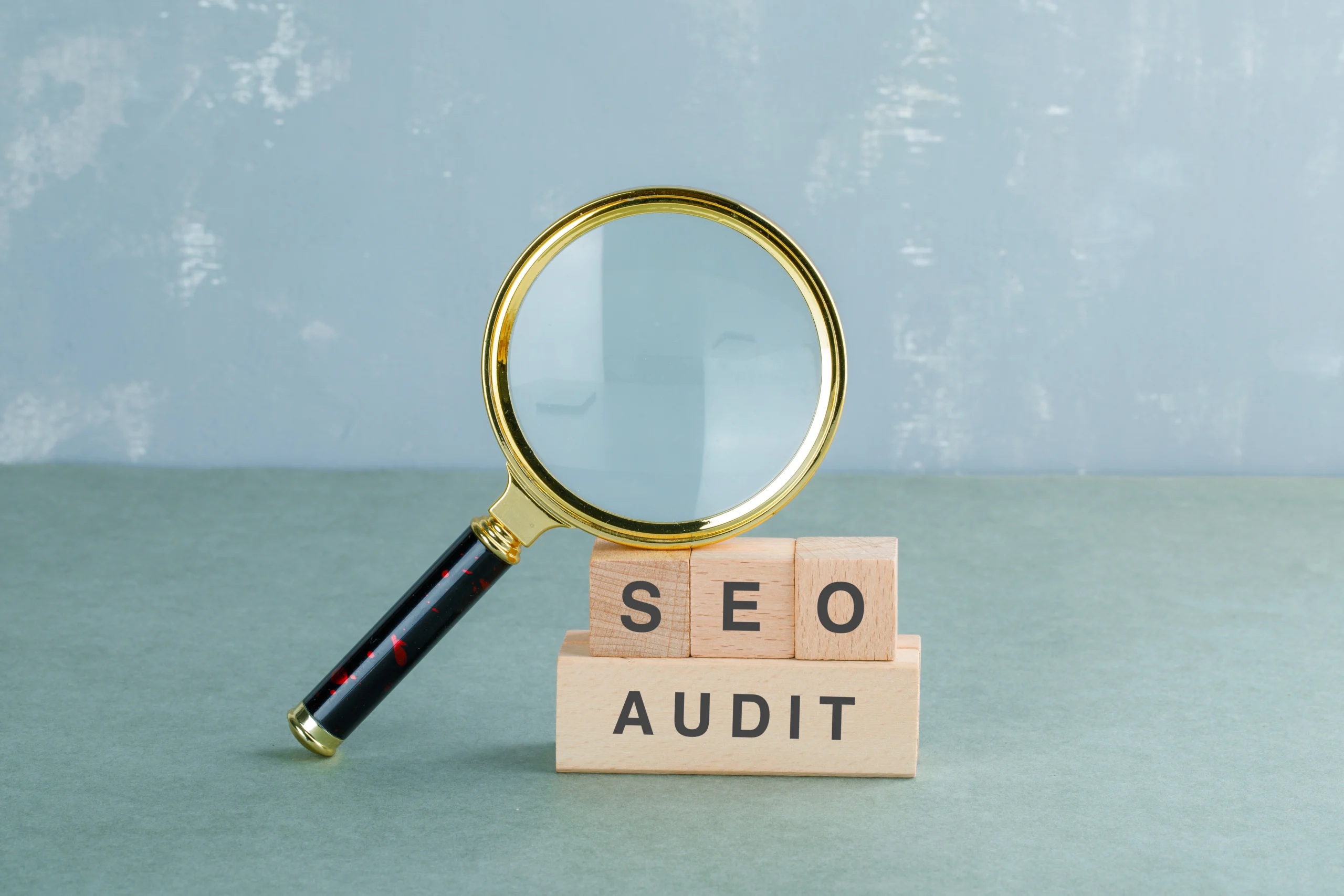 Loupe au-dessus de blocs en bois avec inscription SEO Audit représentant l’analyse et l’audit SEO d’un site web